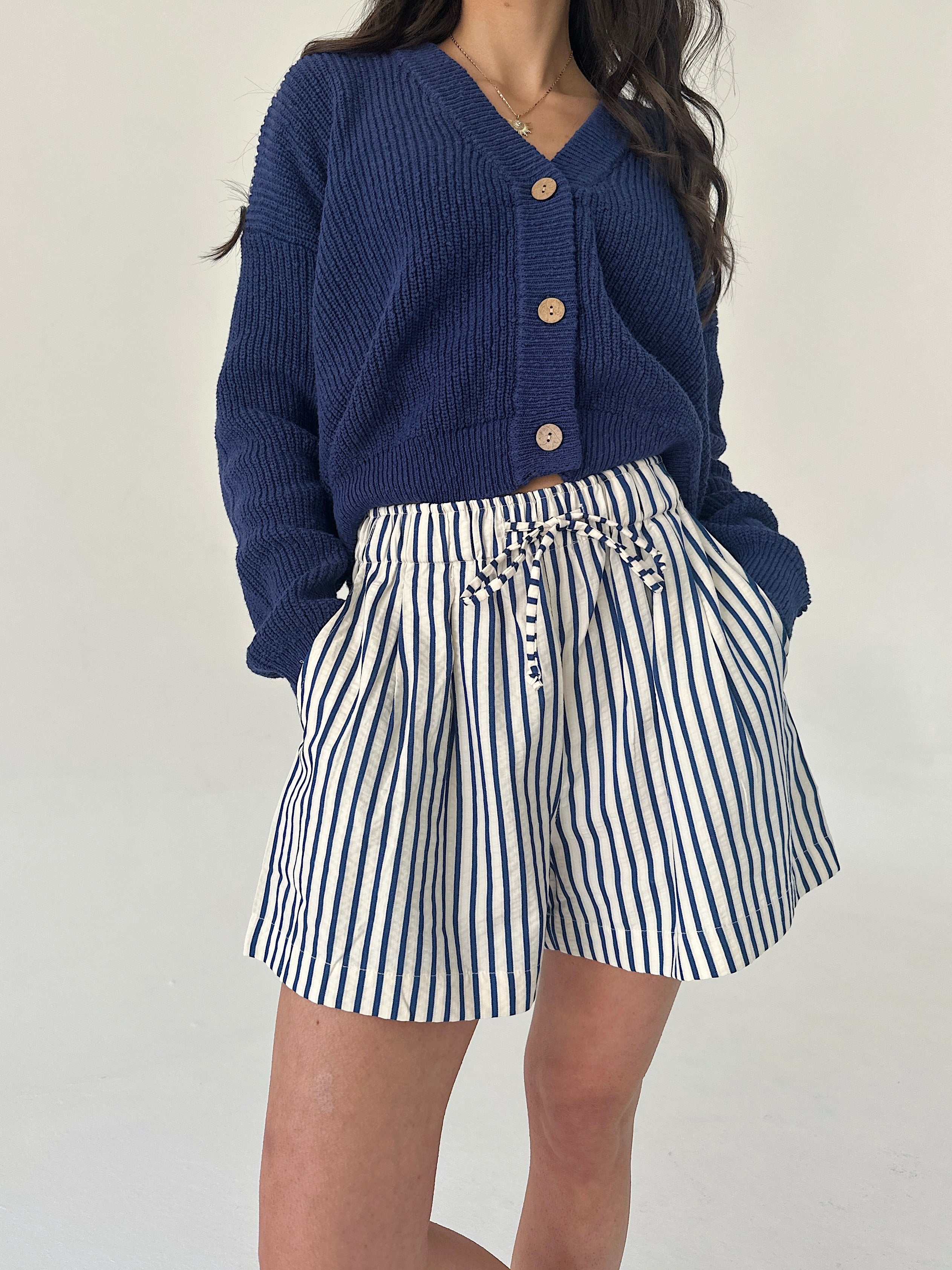 Person wearing a blue cardigan and striped shorts on a plain background