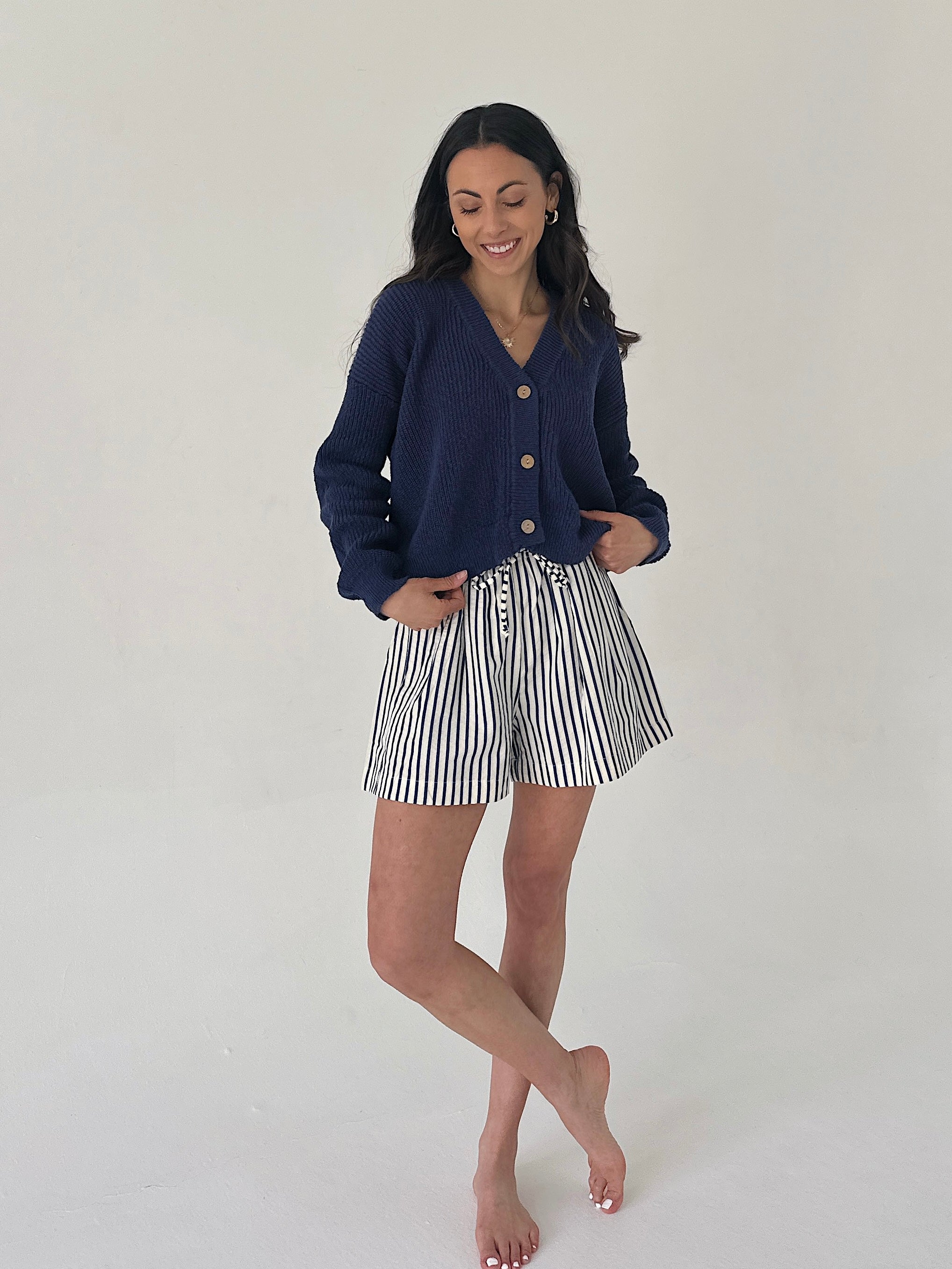 Woman wearing a navy cardigan and striped shorts on a plain background
