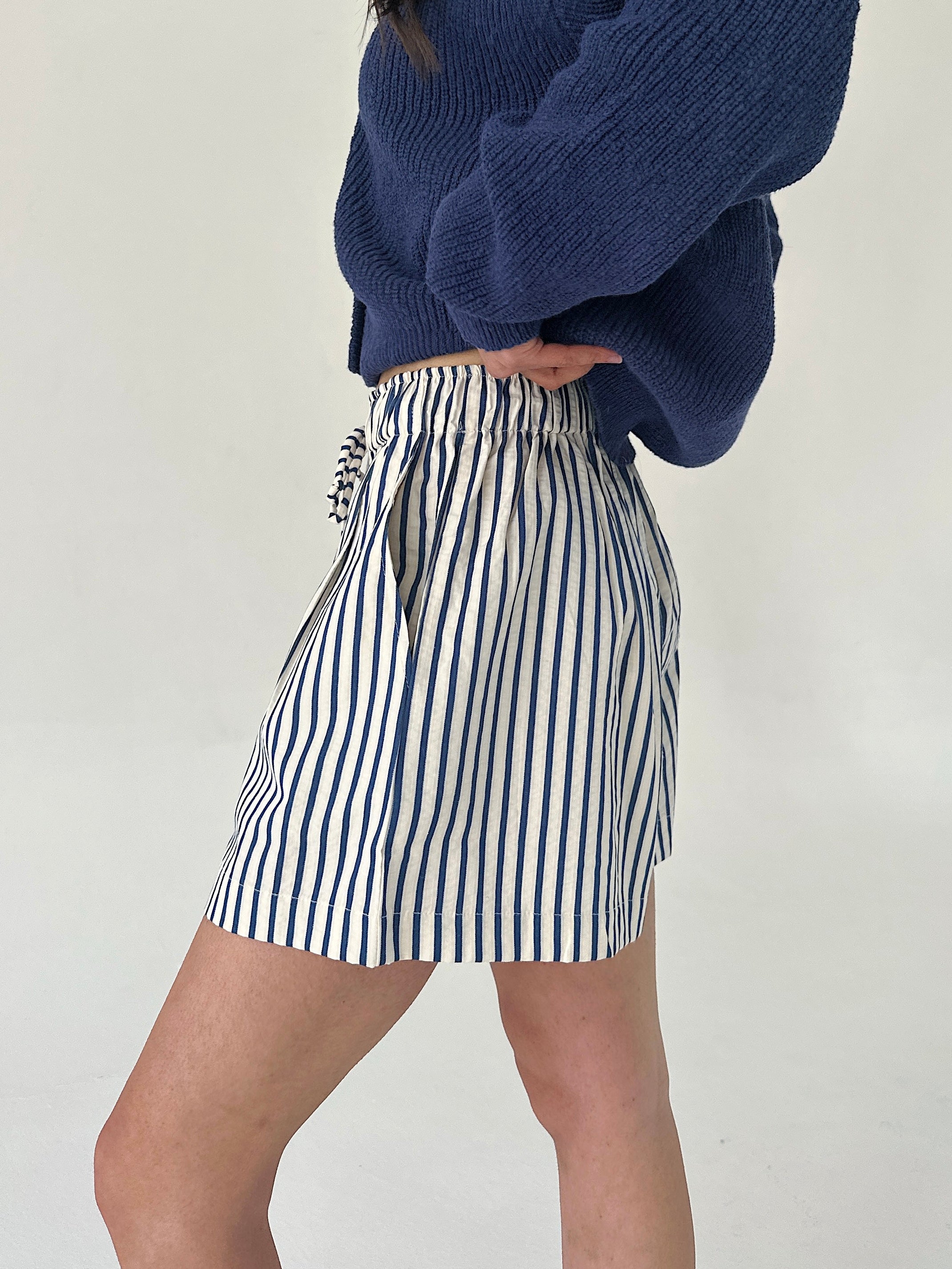 Person wearing a blue sweater and striped skirt on a plain background