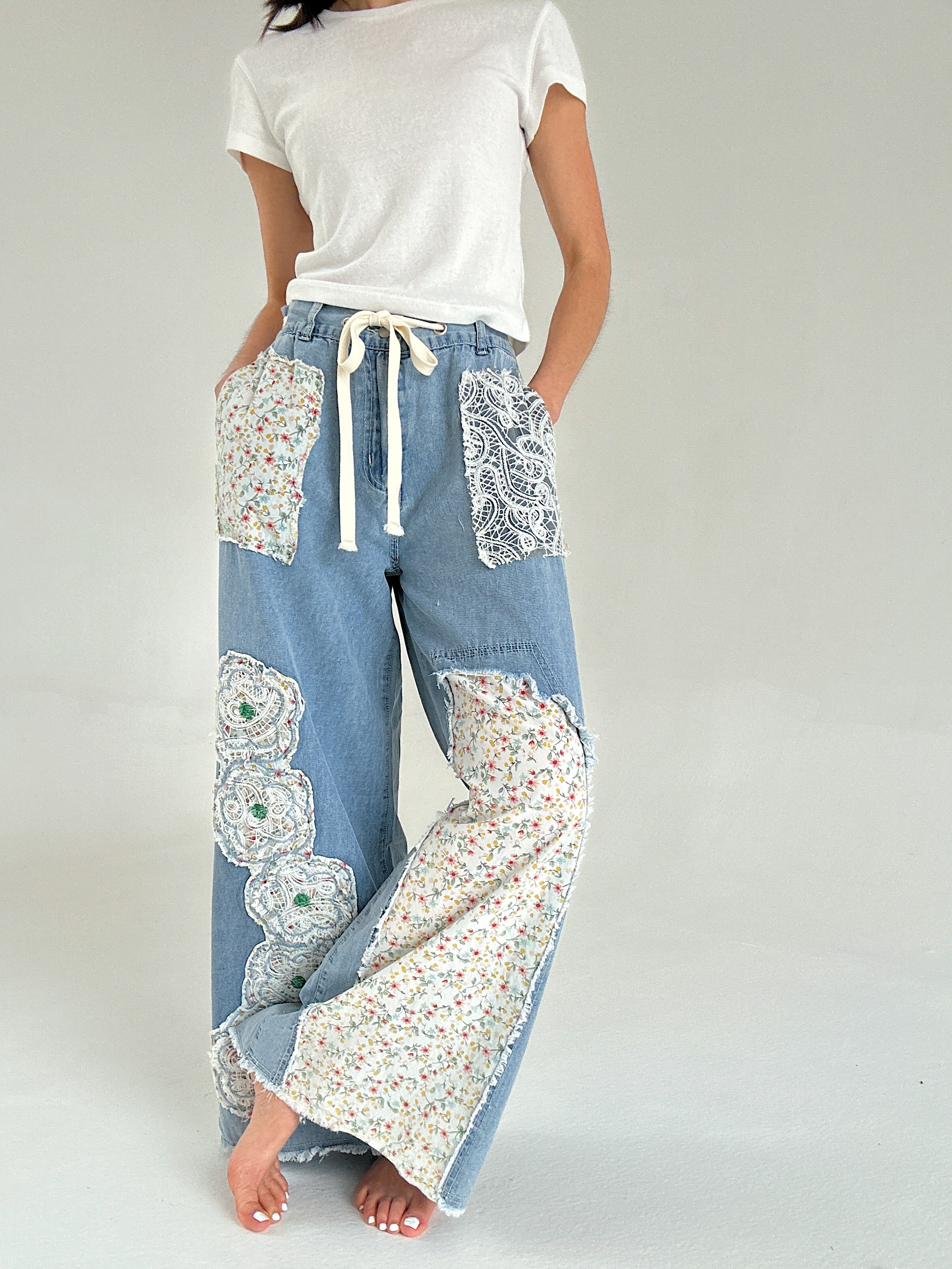 Person wearing light blue denim pants with floral patchwork on a plain background