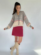 Woman wearing a patterned sweater and red skirt with beige knee-high boots on a white background