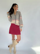 Woman wearing a patterned sweater, red skirt, and beige knee-high boots against a white background