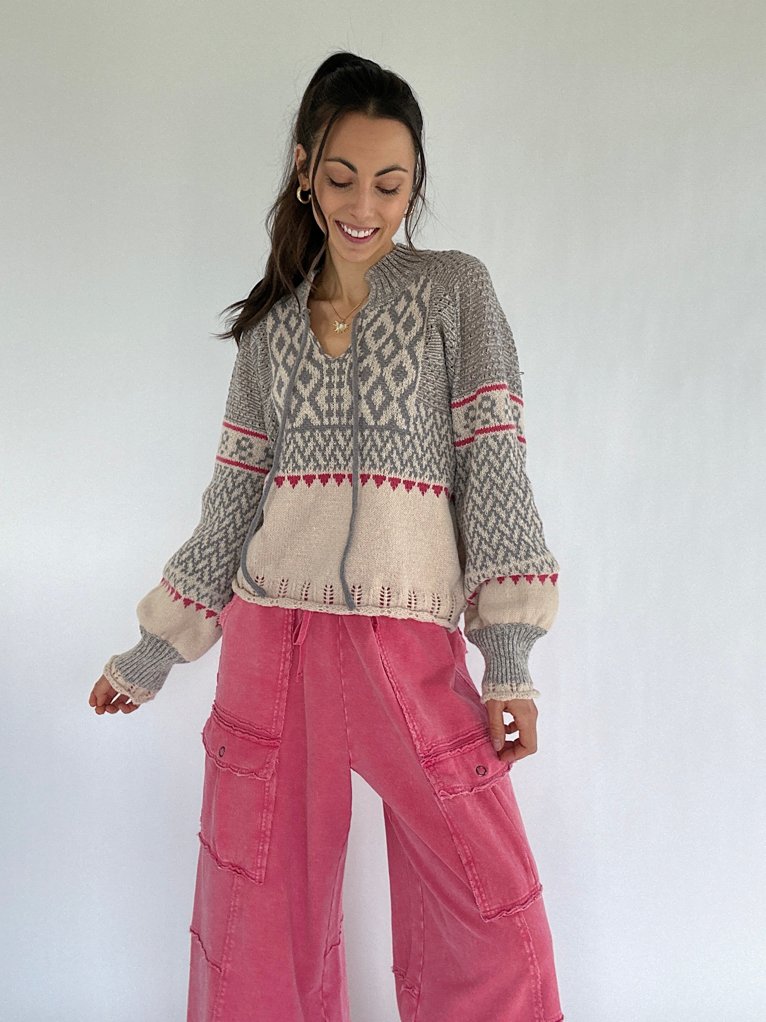 Woman wearing a patterned sweater and pink pants against a white background