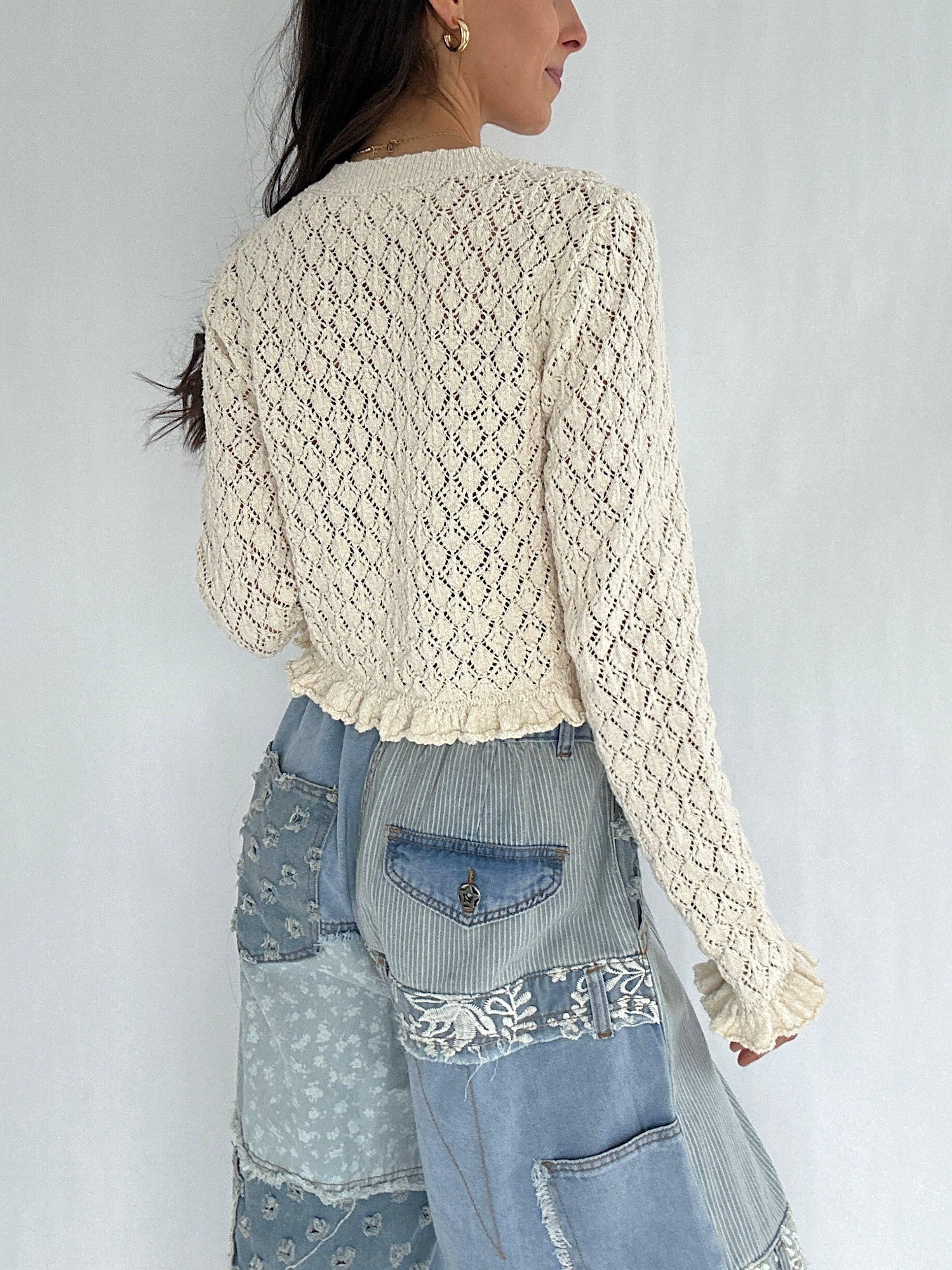 Woman wearing a cream lace top and denim patchwork pants against a white background