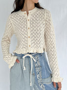 Person wearing a textured beige cardigan over denim pants on a plain background