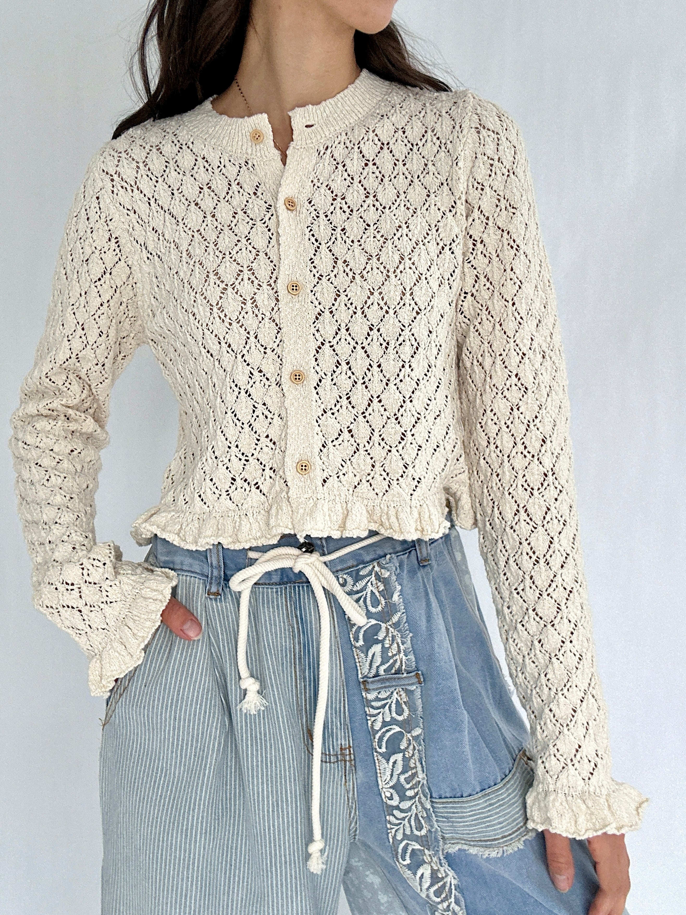 Person wearing a textured beige cardigan over denim pants on a plain background