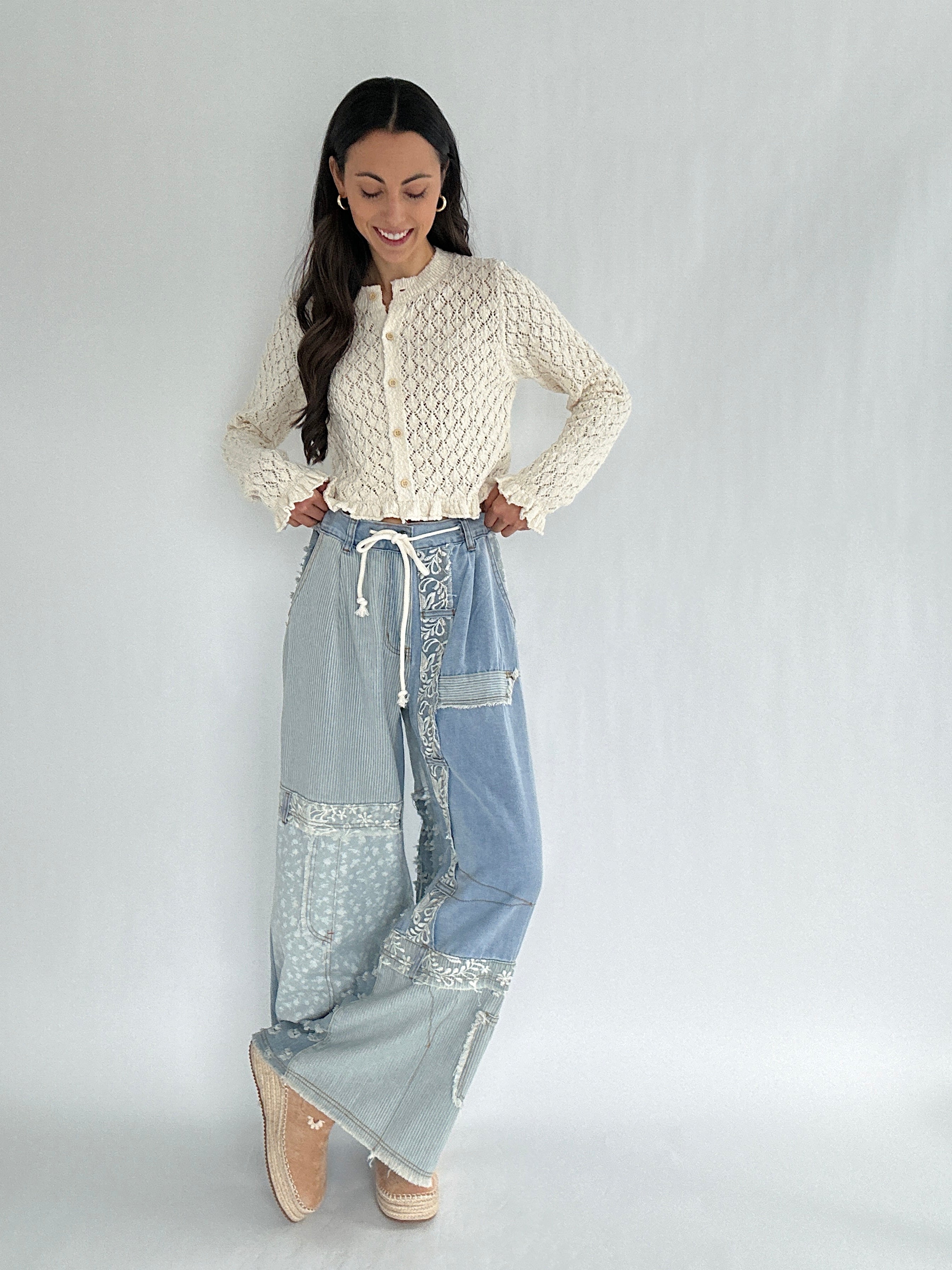 Woman wearing a cream top and light blue pants with lace details on a white background