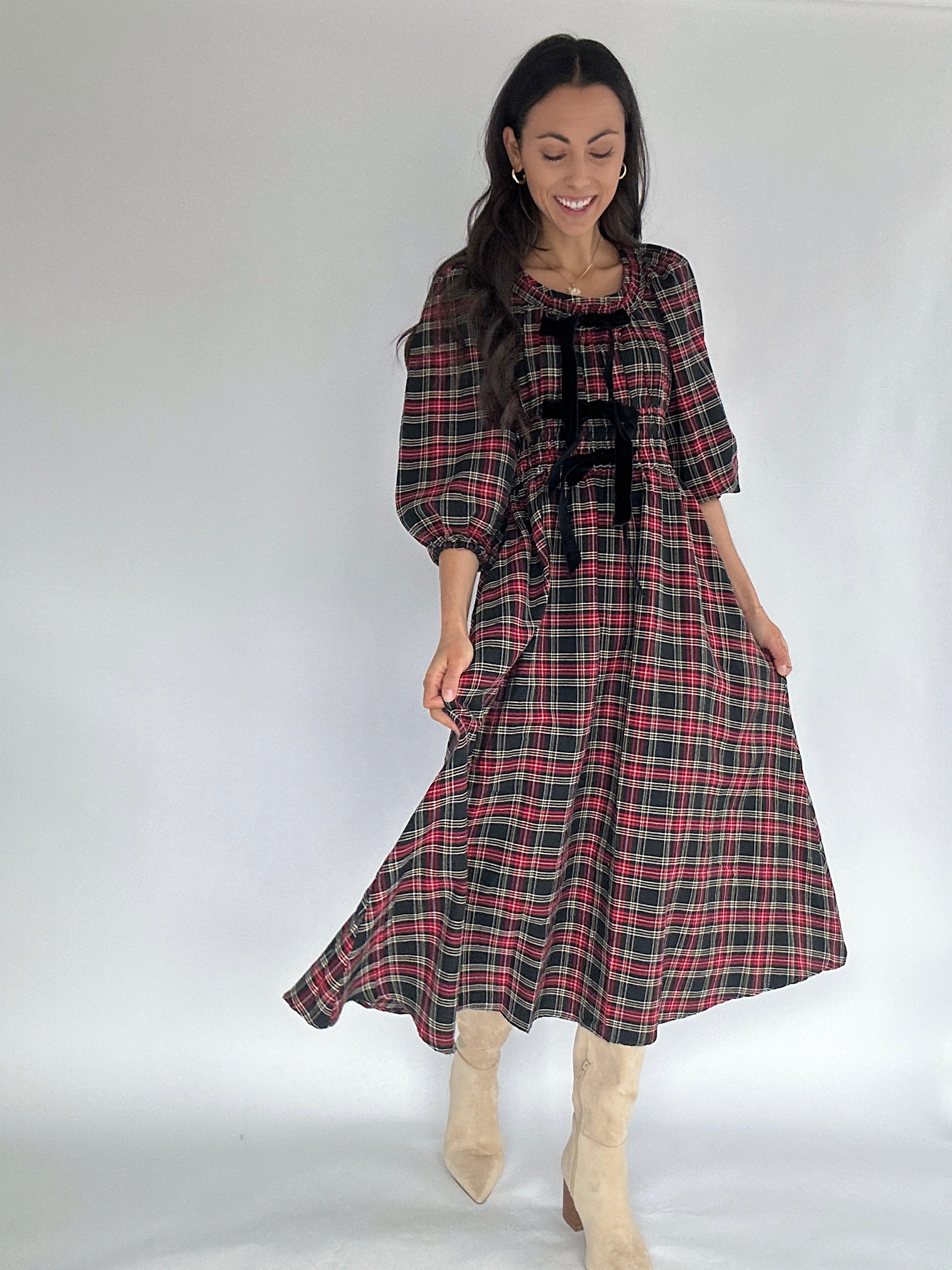 Woman wearing a plaid dress with velvet bow accents on a plain background