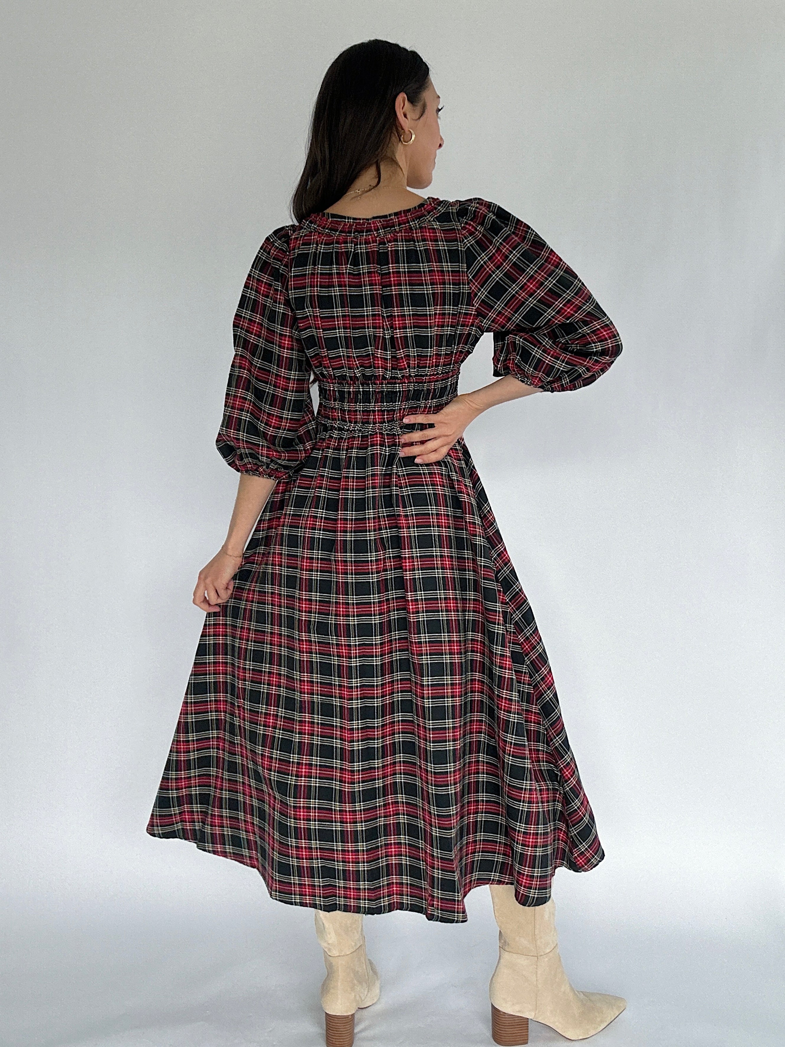 Woman wearing a plaid dress with a plain background showing back