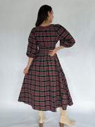 Woman wearing a plaid dress with a plain background showing back
