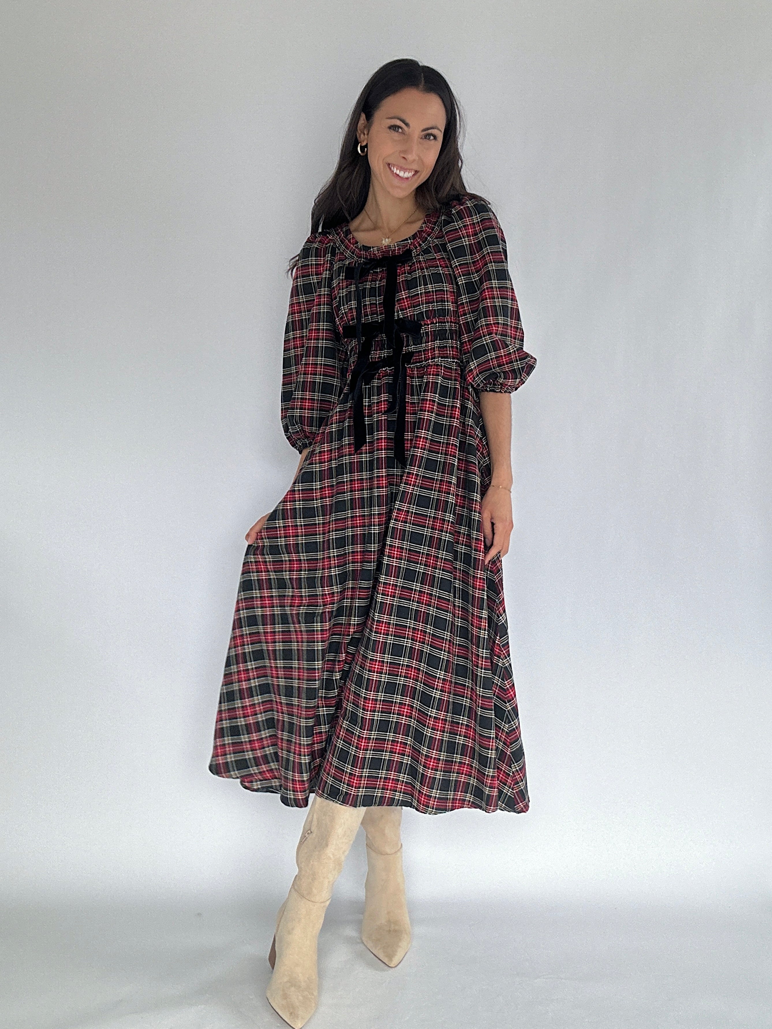 Woman wearing a plaid dress with black bow accents at top on a white background