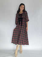 Woman wearing a plaid dress with black bow accents at top on a white background