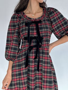 Plaid dress with black bow accents on a plain background showing round neckline