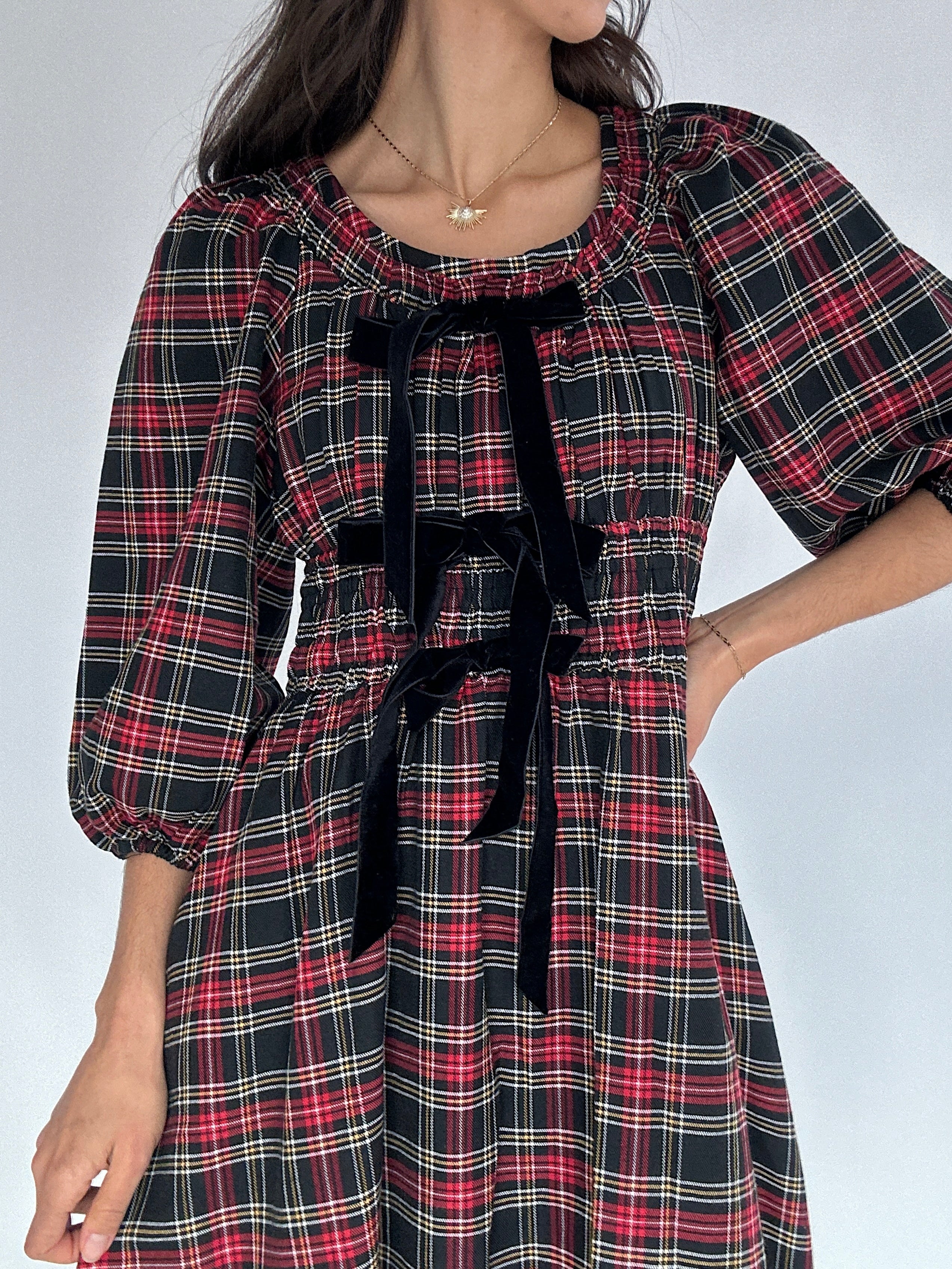 Plaid dress with black bow accents on a plain background showing round neckline