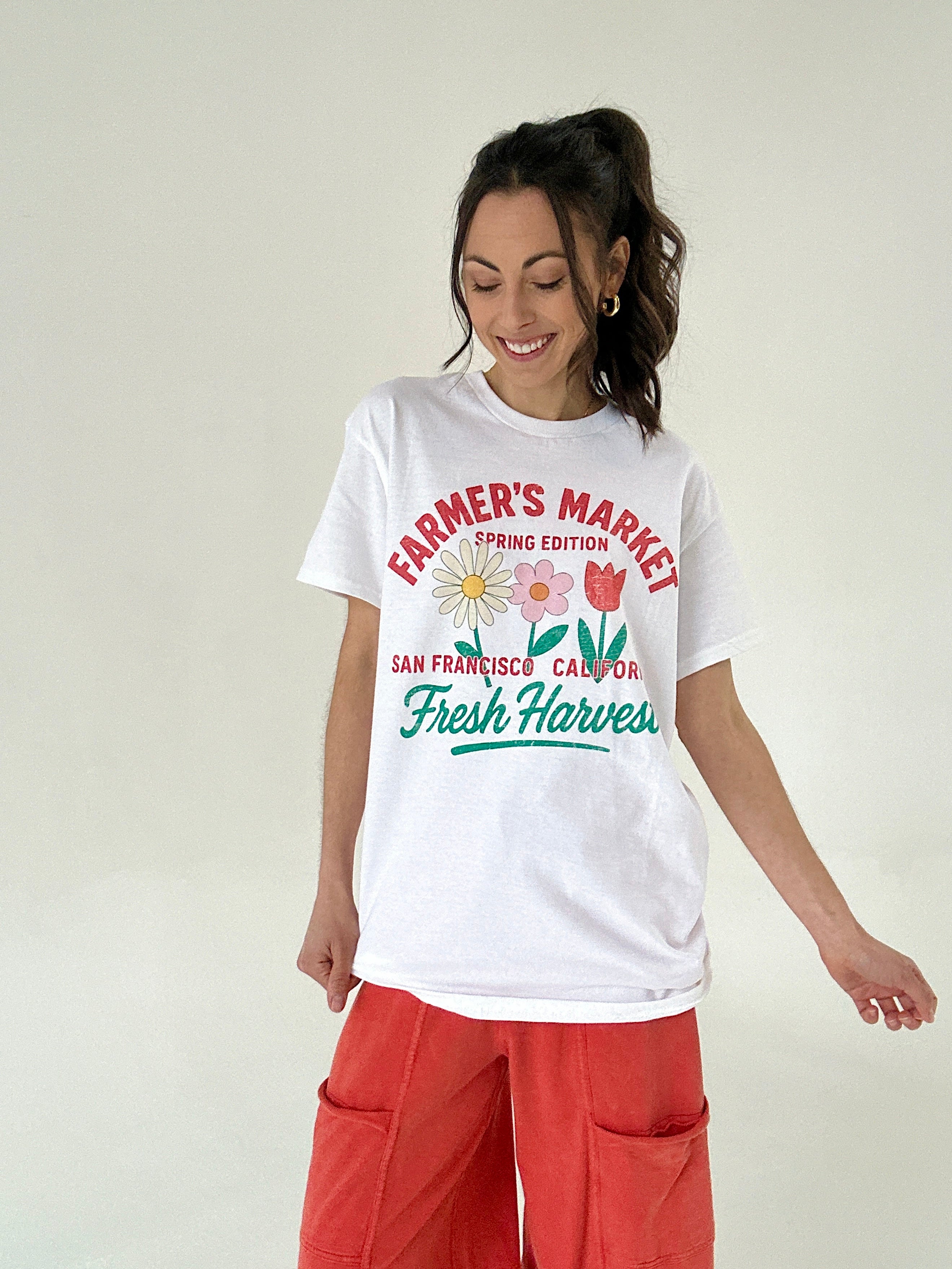 Woman wearing a white t-shirt with 'Farmer's Market' text and graphics on a plain background