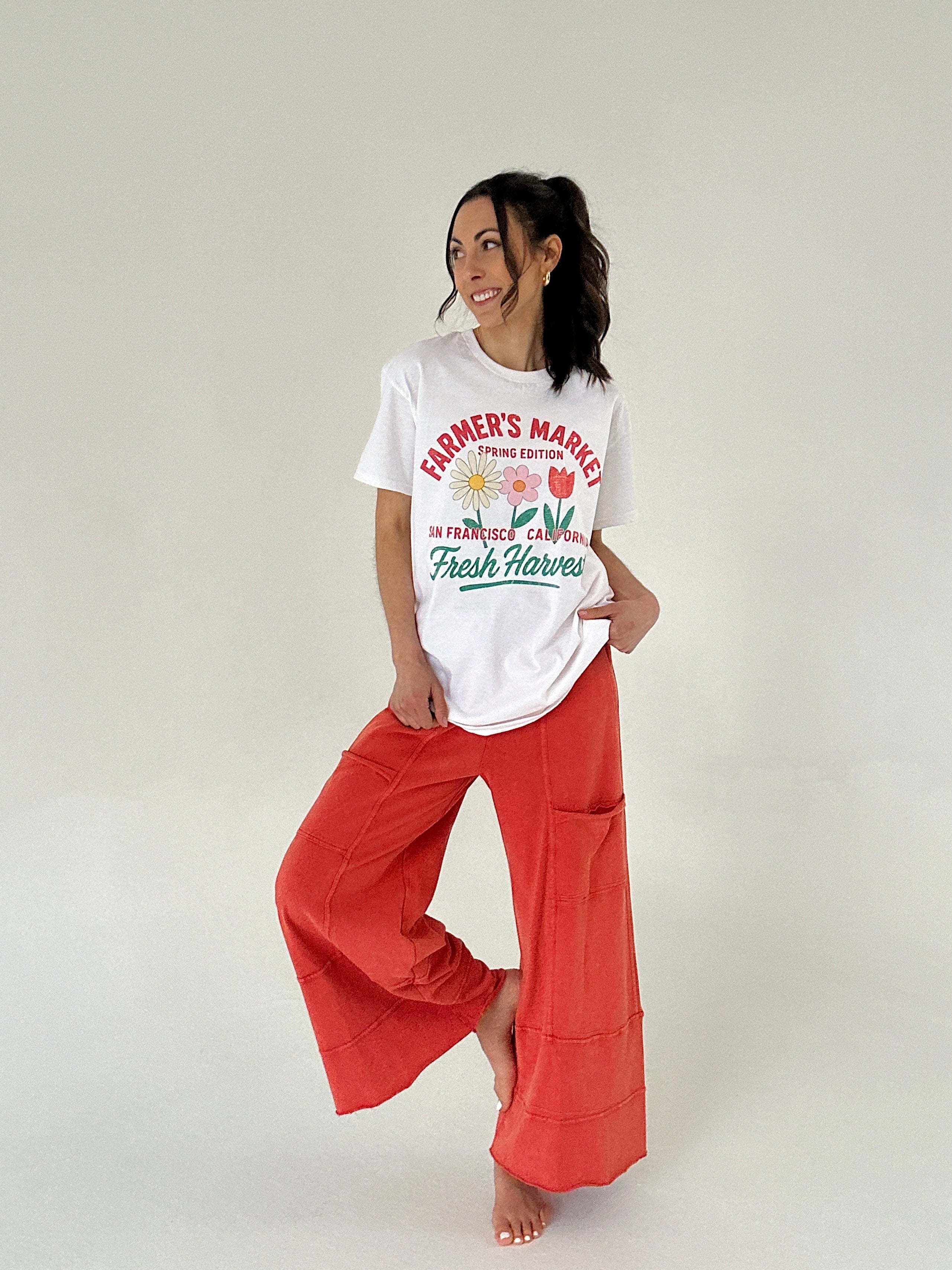 Woman wearing a white t-shirt with graphics and text, paired with red pants on a plain background