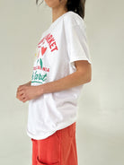 Person wearing a white t-shirt with colorful graphics and text on a plain background
