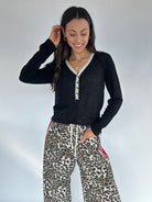 Woman wearing a black long-sleeve top with lace trim and leopard print pants against a white background