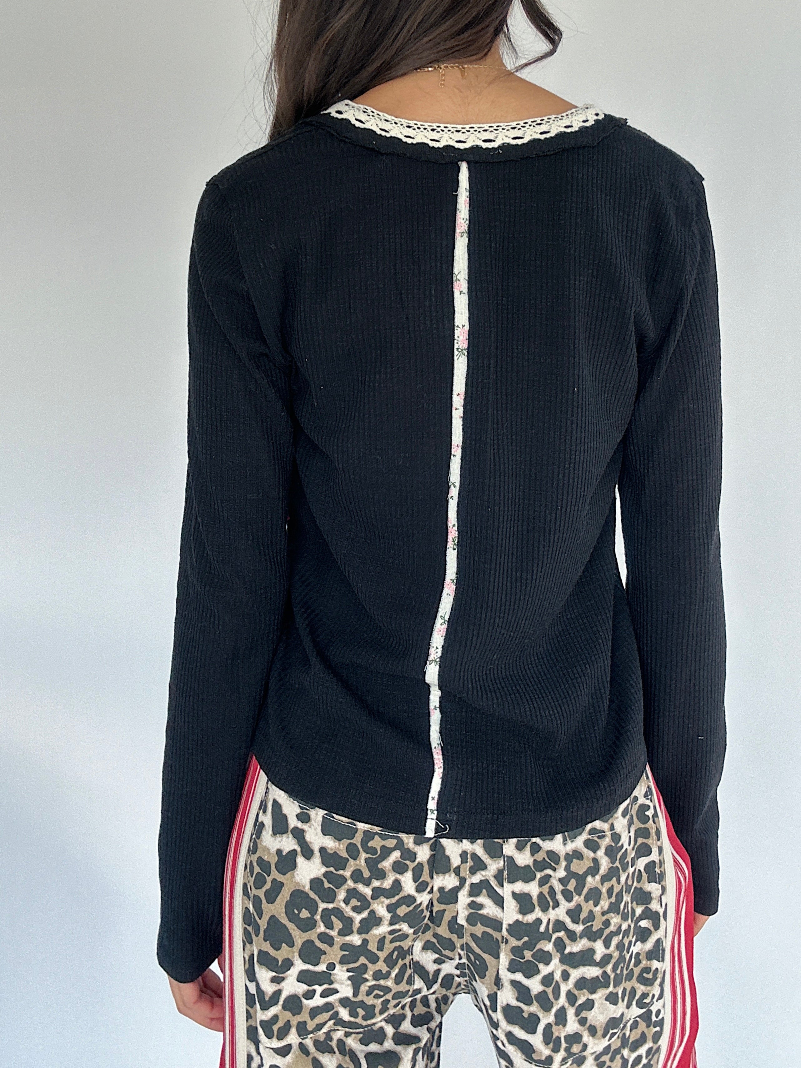 Person wearing a black long-sleeve top with white trim down the back and leopard print pants on a plain background 