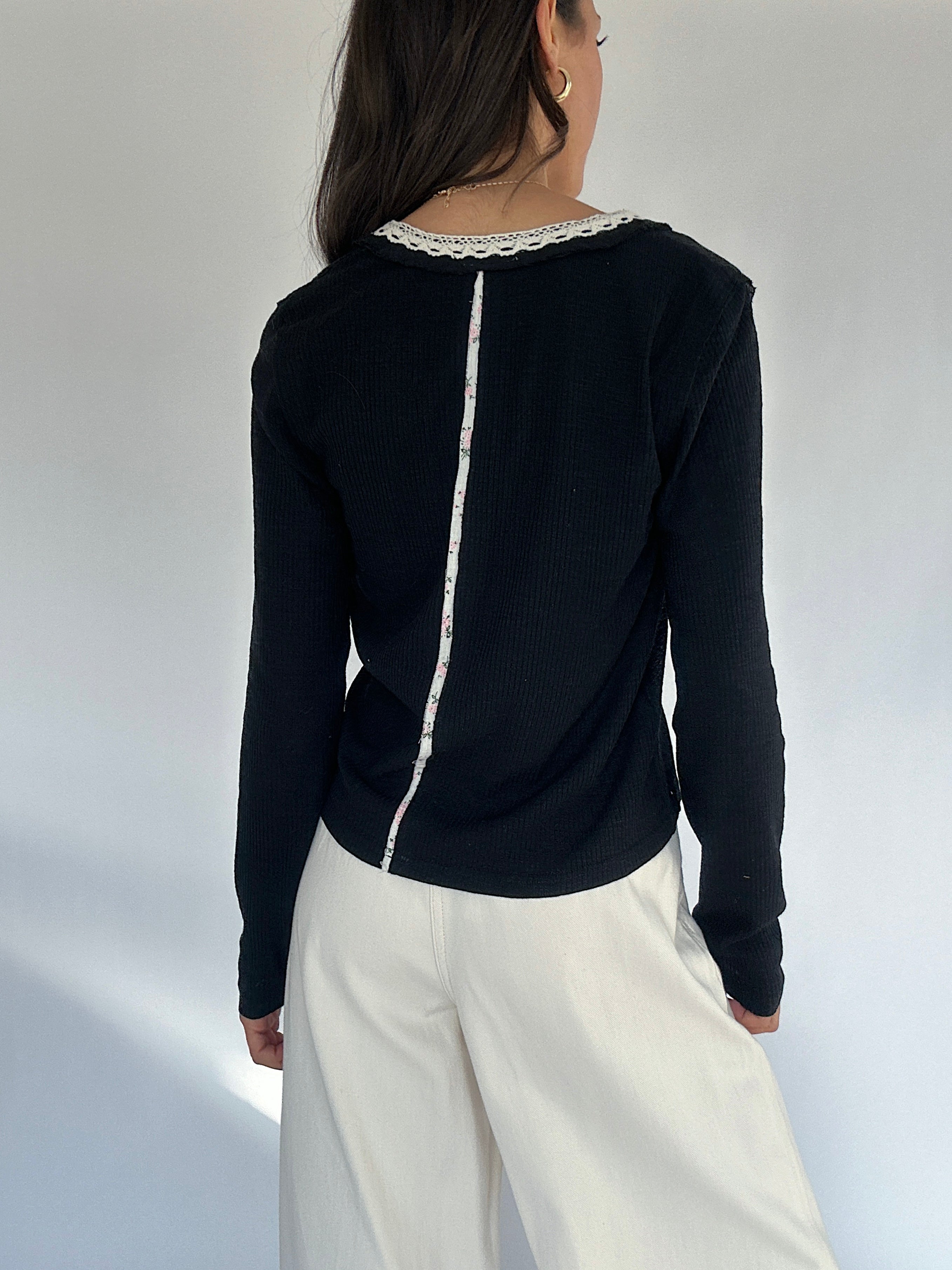 Person wearing a black long-sleeve top with white lace trim on a plain background