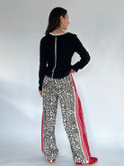 Woman wearing a black top and leopard print pants with red stripes on a white background