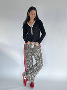 Woman wearing a black top and leopard print pants with red stripes on a white background