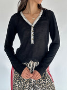 Person wearing a black long-sleeve top with lace trim and leopard print pants against a white background