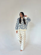 A woman modeling a long-sleeve crewneck sweater with a navy blue fish pattern on an off-white background, and  off-white pants with a navy blue polka dot pattern, set against a plain light gray studio background.
