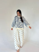 A woman modeling a cream sweater with a navy fish pattern and cream pants with navy polka dots, set against a plain light gray studio background.