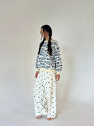 A woman modeling long-sleeve crewneck sweater with a navy blue fish pattern on an off-white background, and wide-leg pants with a navy blue polka dot pattern on an off-white background, set against a plain light gray studio backdrop.