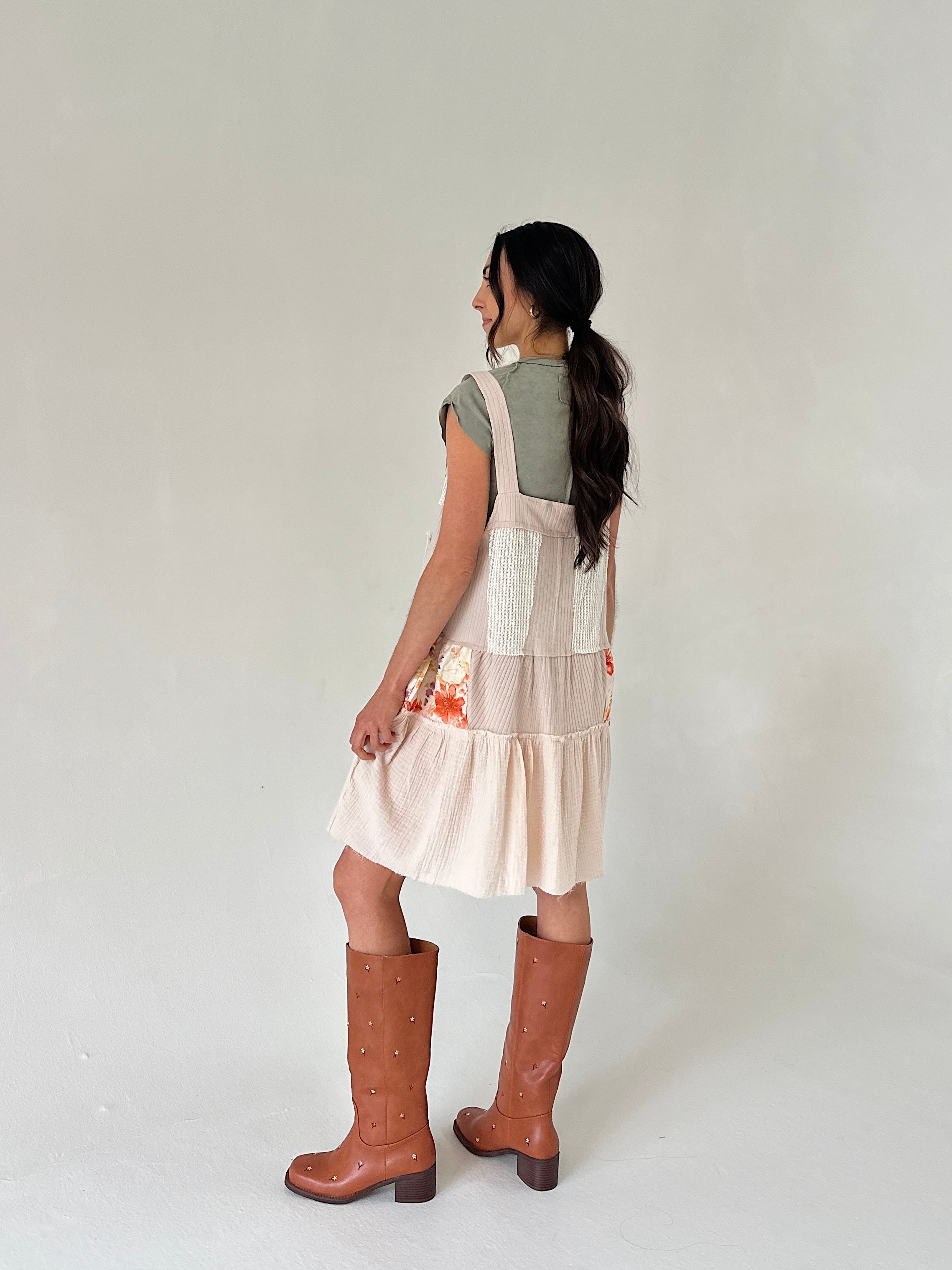 Person wearing a layered dress with a green top and beige skirt, standing against a plain background.