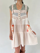 Person wearing a beige overalls dress with floral sleeves on a plain background
