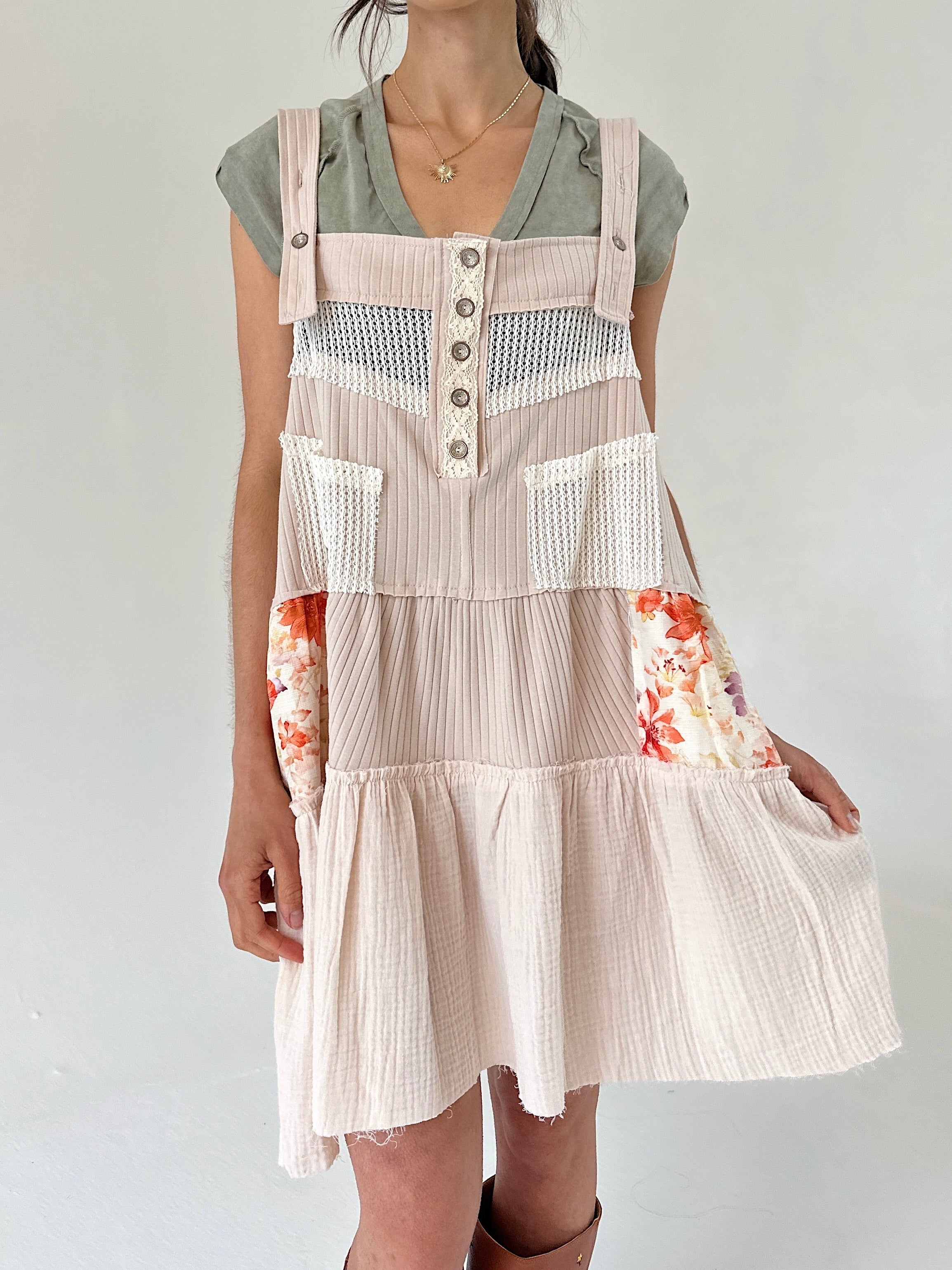 Person wearing a beige overalls dress with floral sleeves on a plain background