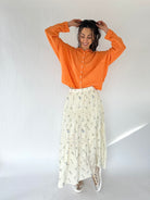 Woman wearing an orange shirt and white floral skirt against a white background