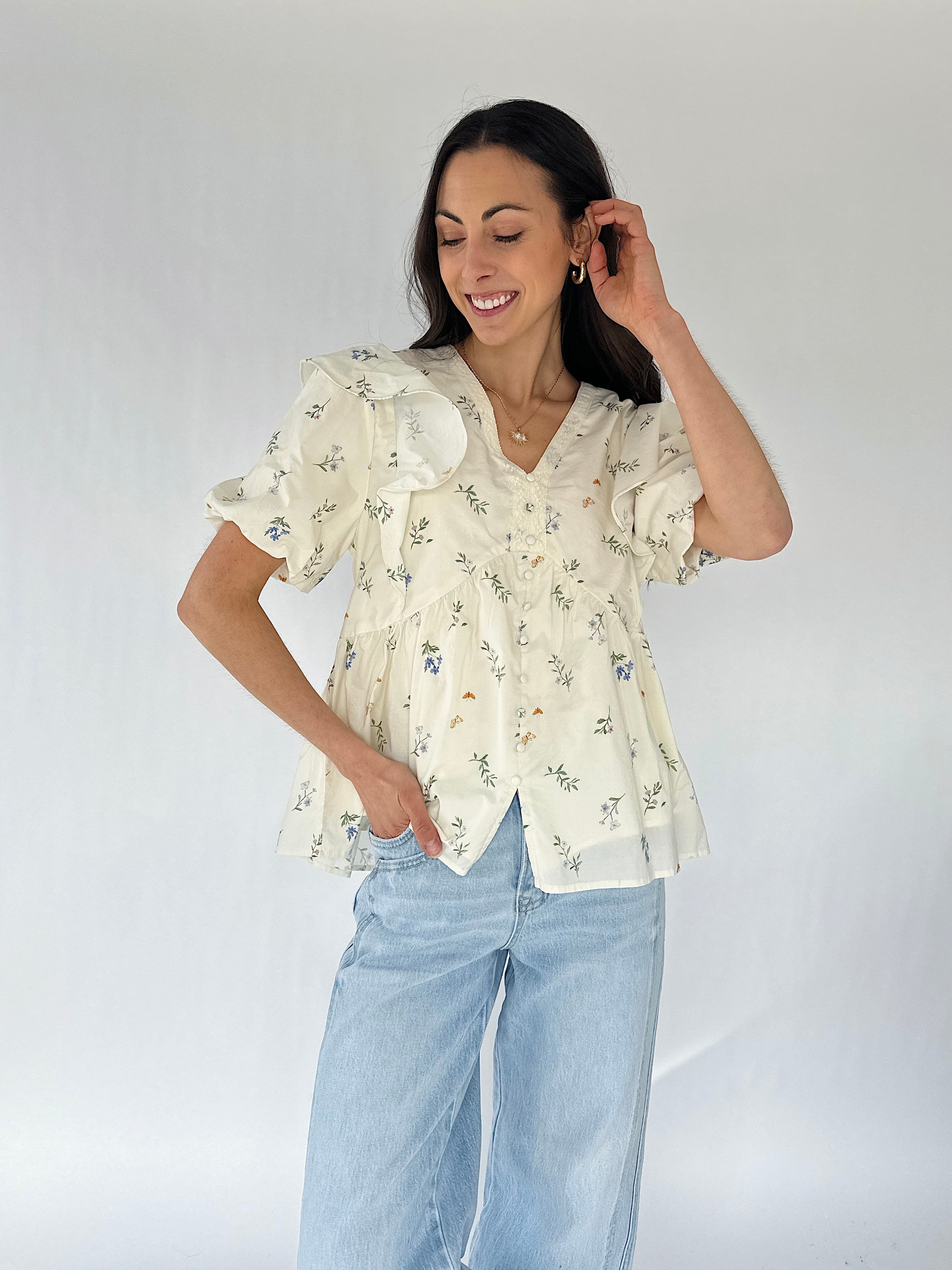 Woman wearing a floral blouse and light blue jeans against a white background