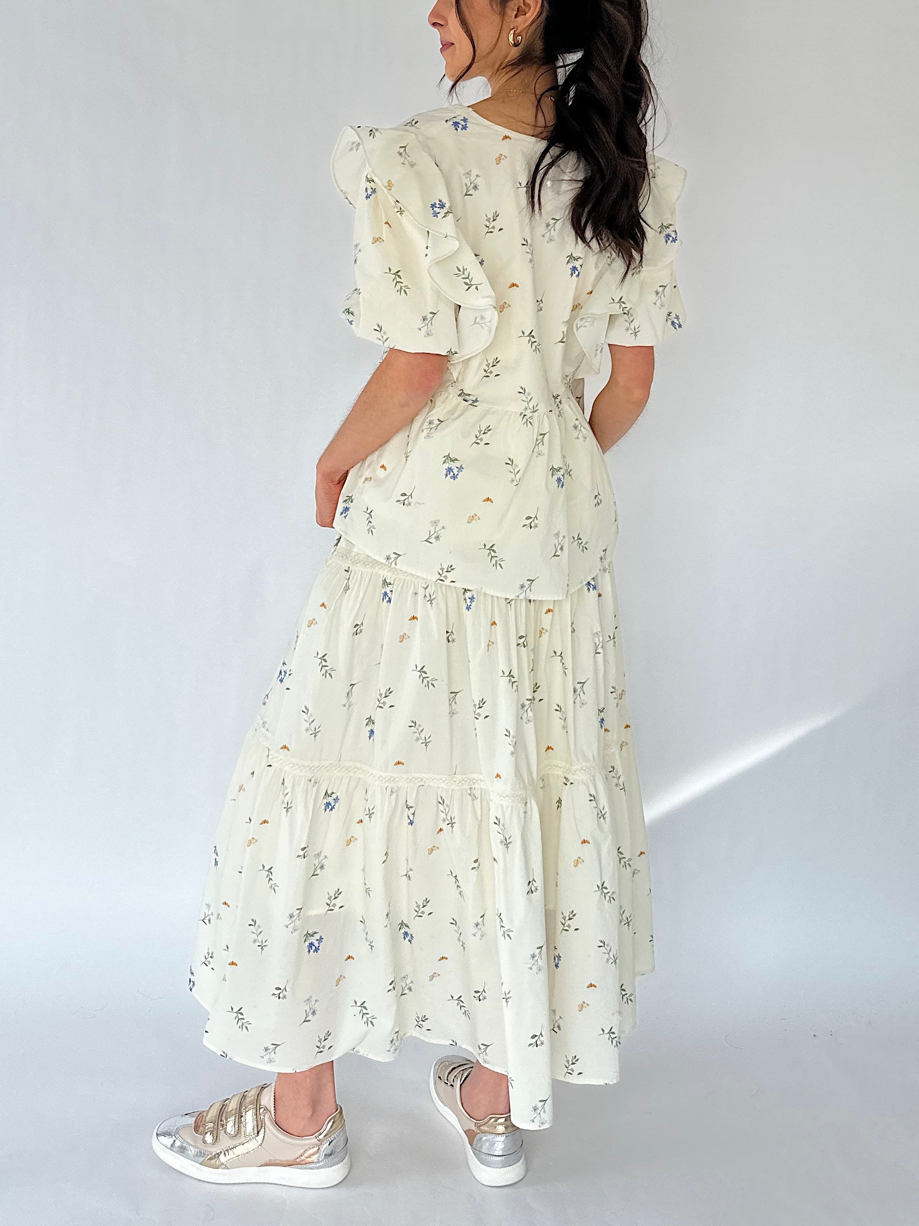 Woman wearing a floral maxi skirt and matching top from back on a white background