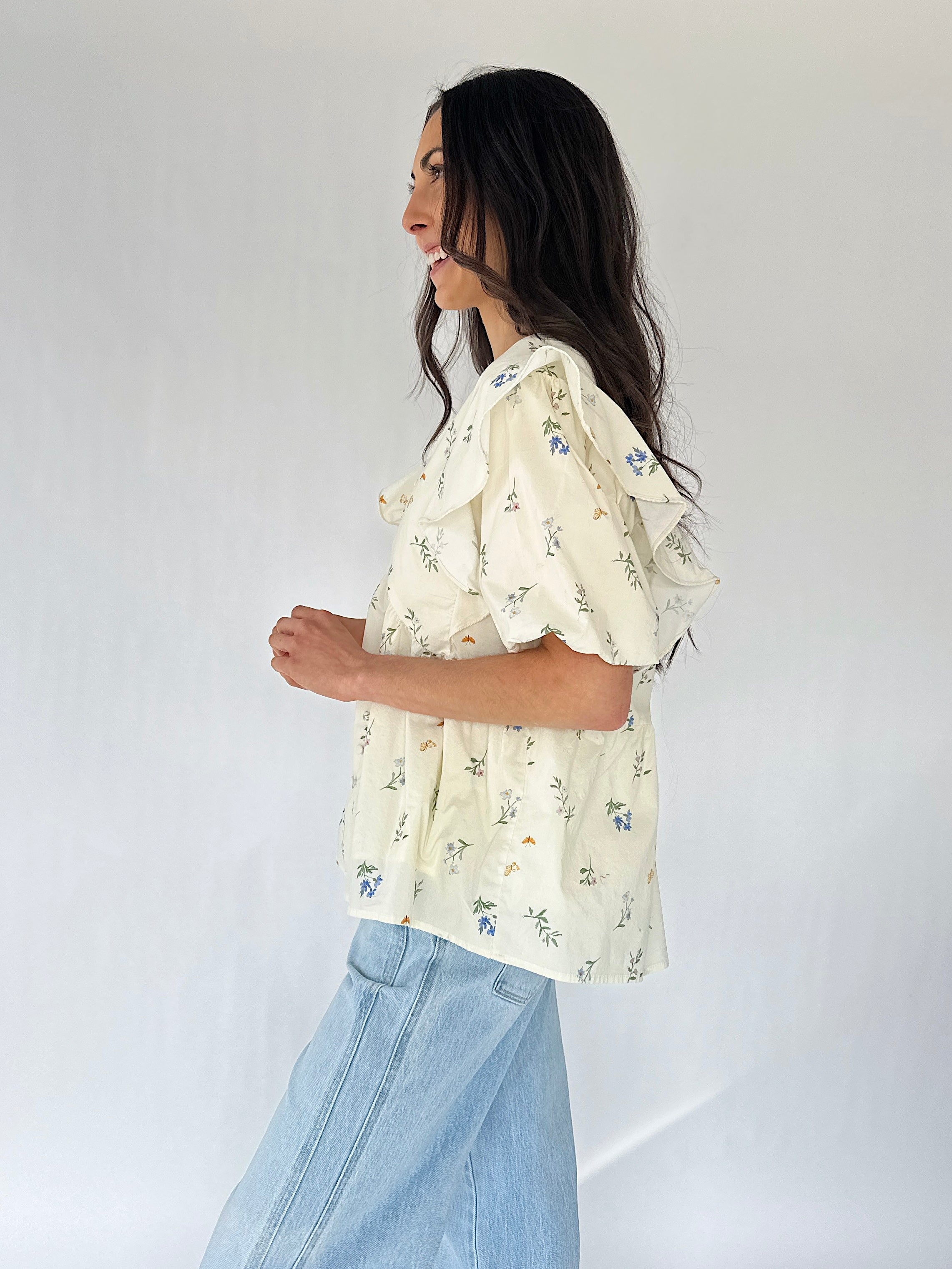 Woman wearing a cream floral blouse and light blue jeans against a white background
