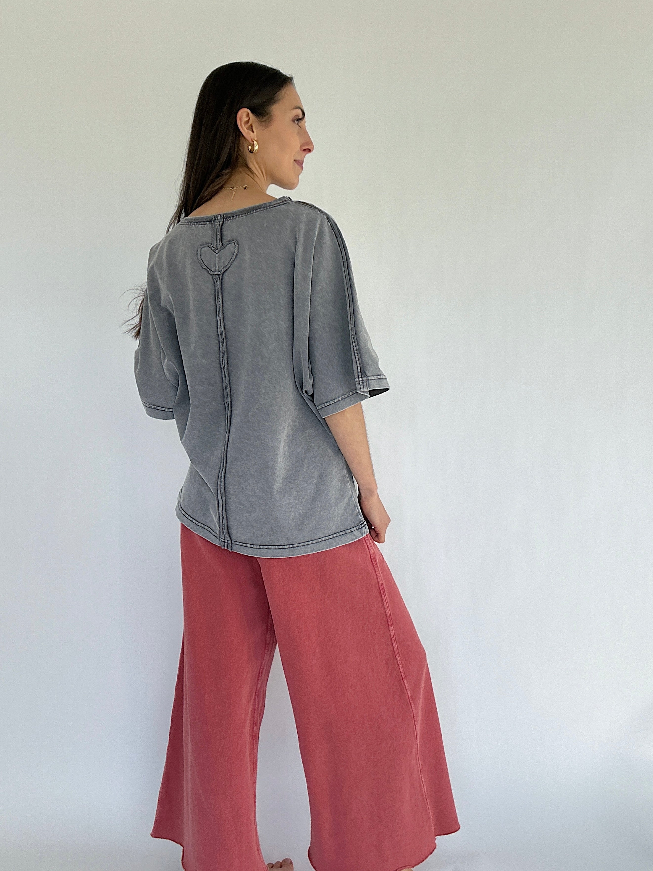 Woman wearing a gray top and pink pants against a white background showing the back