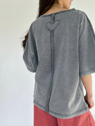 Person wearing a gray mineral washed top with a heart design on the back against a white background