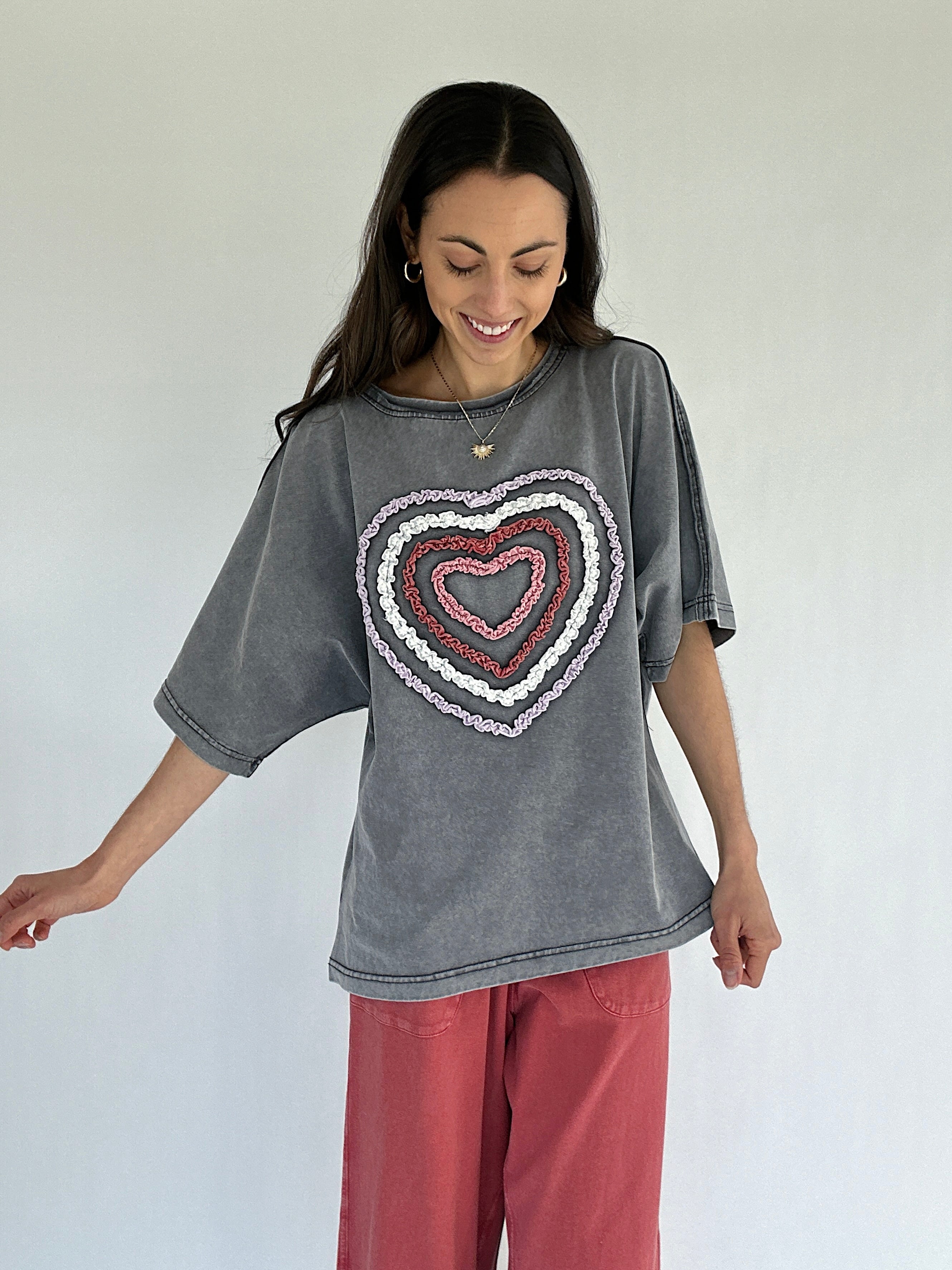 Woman wearing a gray t-shirt with a heart design on a plain background