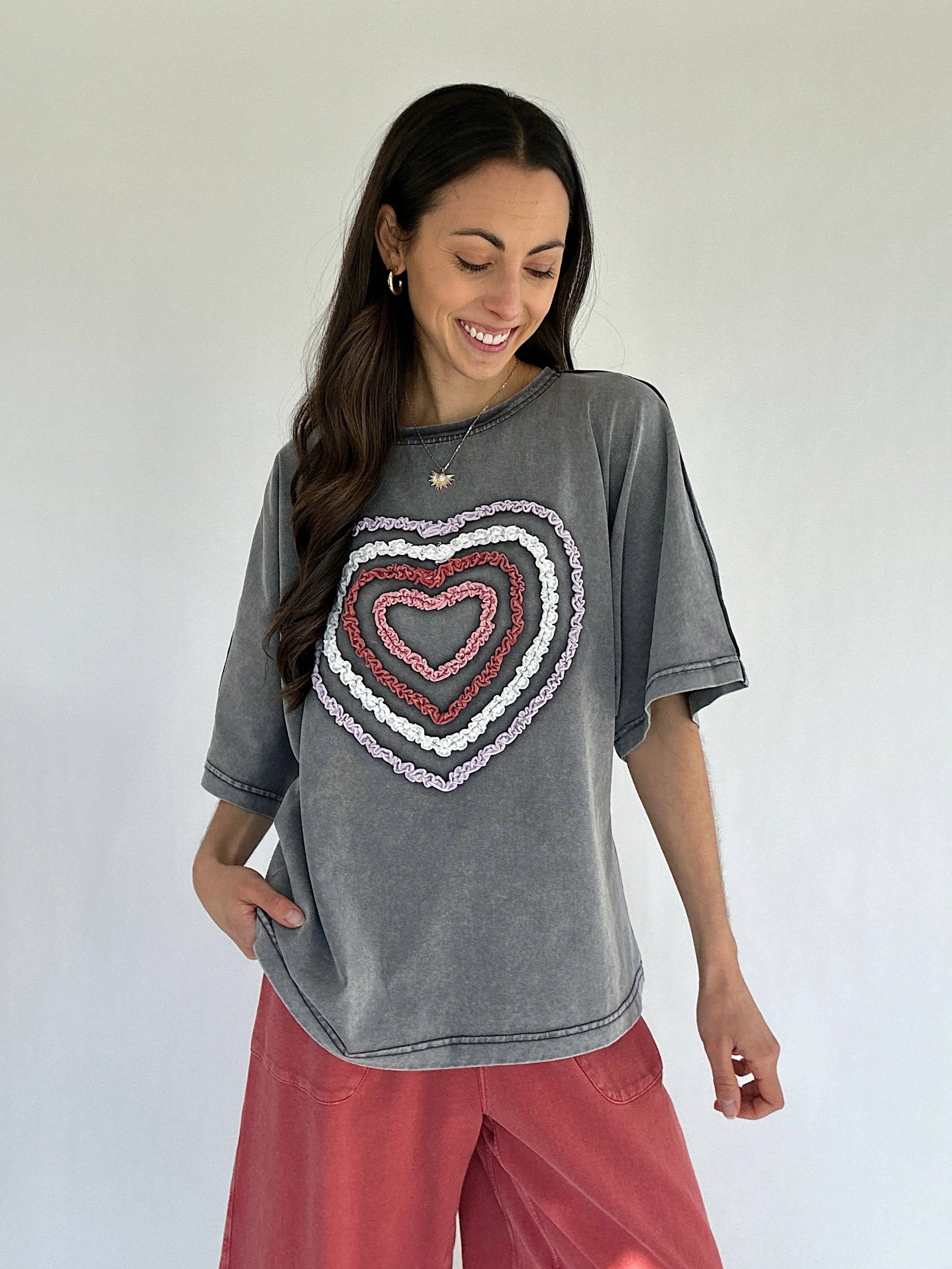 Woman wearing a gray t-shirt with a colorful heart design on a plain background