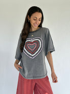 Woman wearing a gray t-shirt with a colorful heart design on a plain background