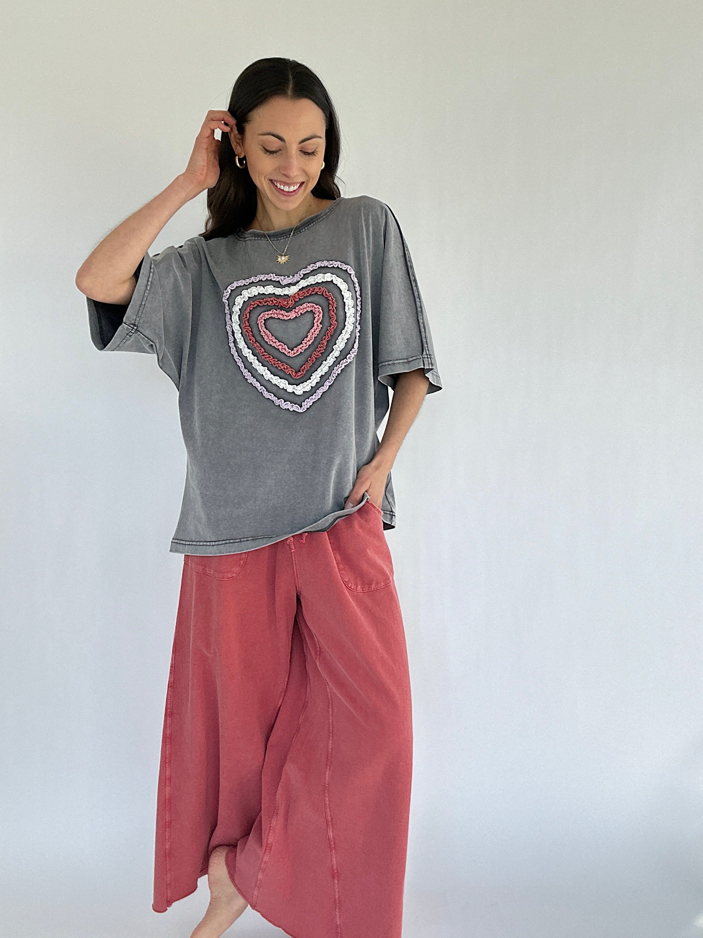 Woman wearing a gray t-shirt with a heart design and pink pants against a white background