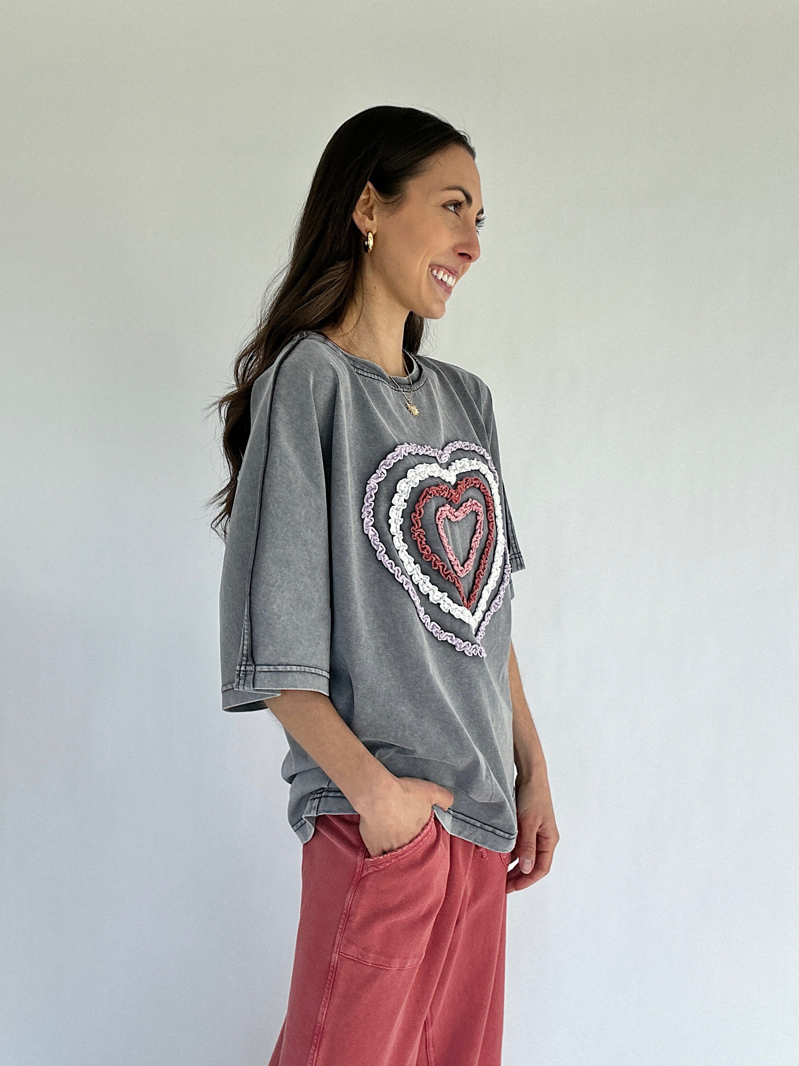 Woman wearing a gray oversized t-shirt with a heart design, standing against a plain background