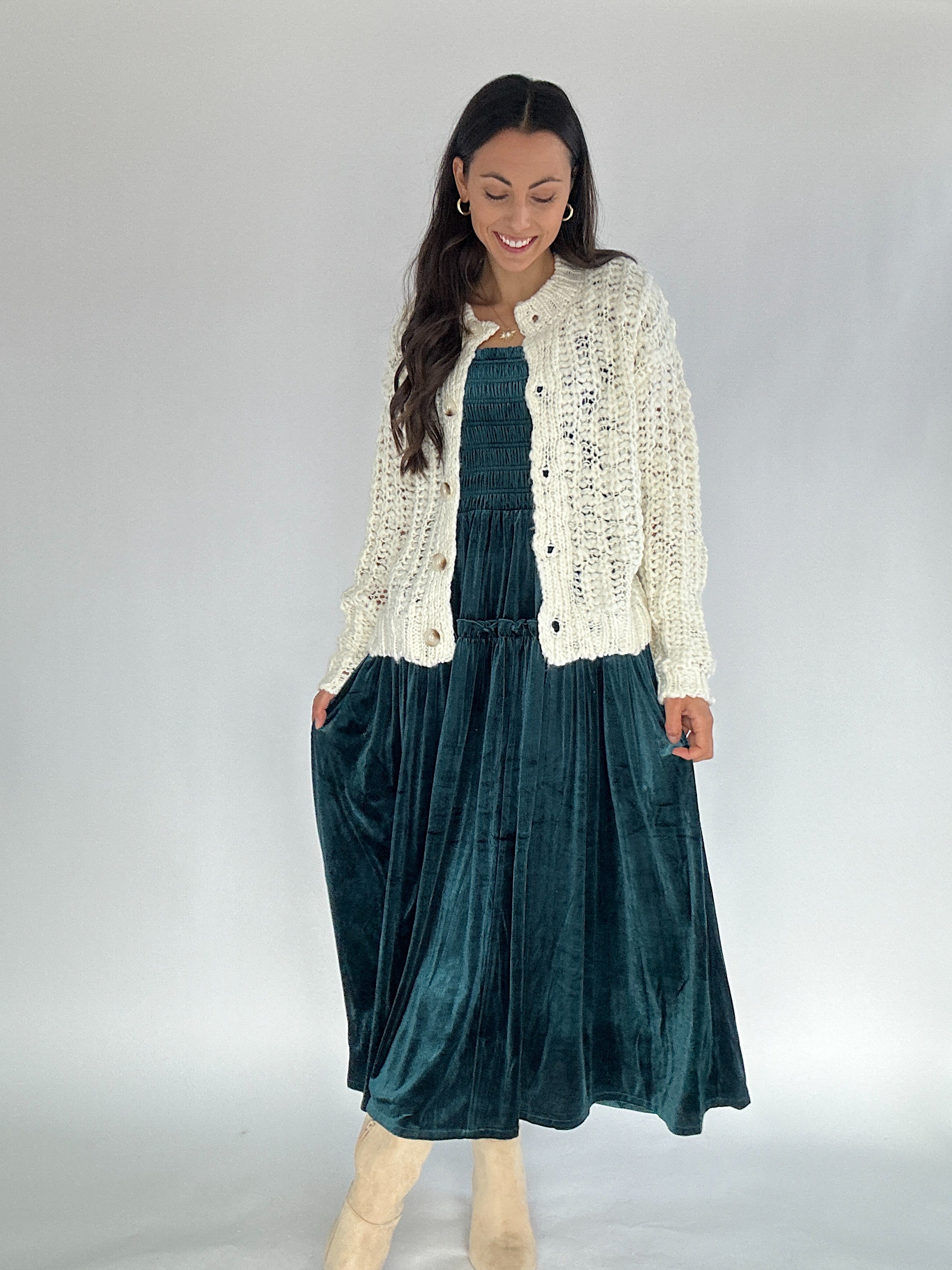 Woman wearing a white cardigan over a green velvet dress on a plain background