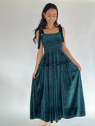 Woman wearing a teal velvet dress against a white background