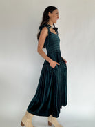 Woman wearing a dark green dress with a white background showing side with pockets