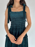 Person wearing a green smocked dress with bow tie straps on a plain background