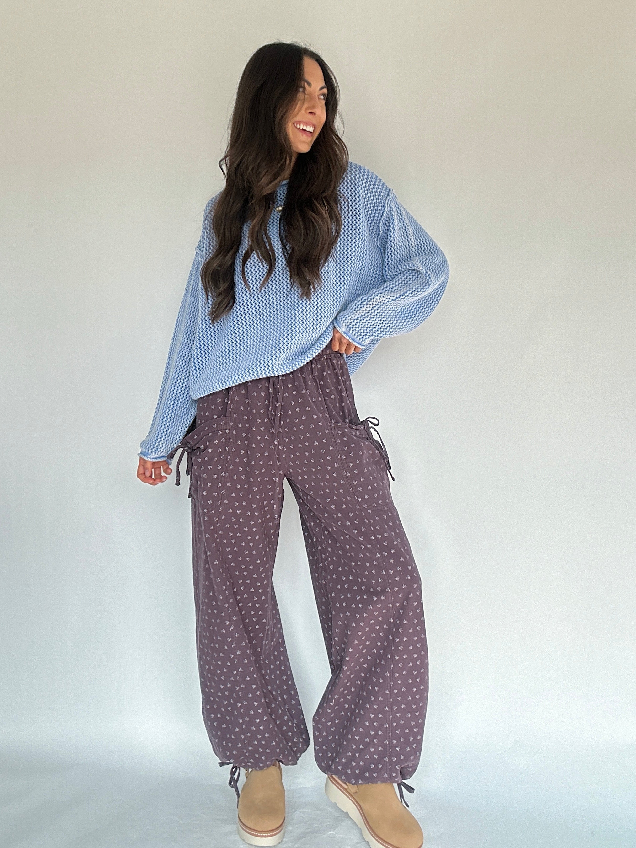 Woman wearing a blue patterned top and purple polka dot pants against a white background