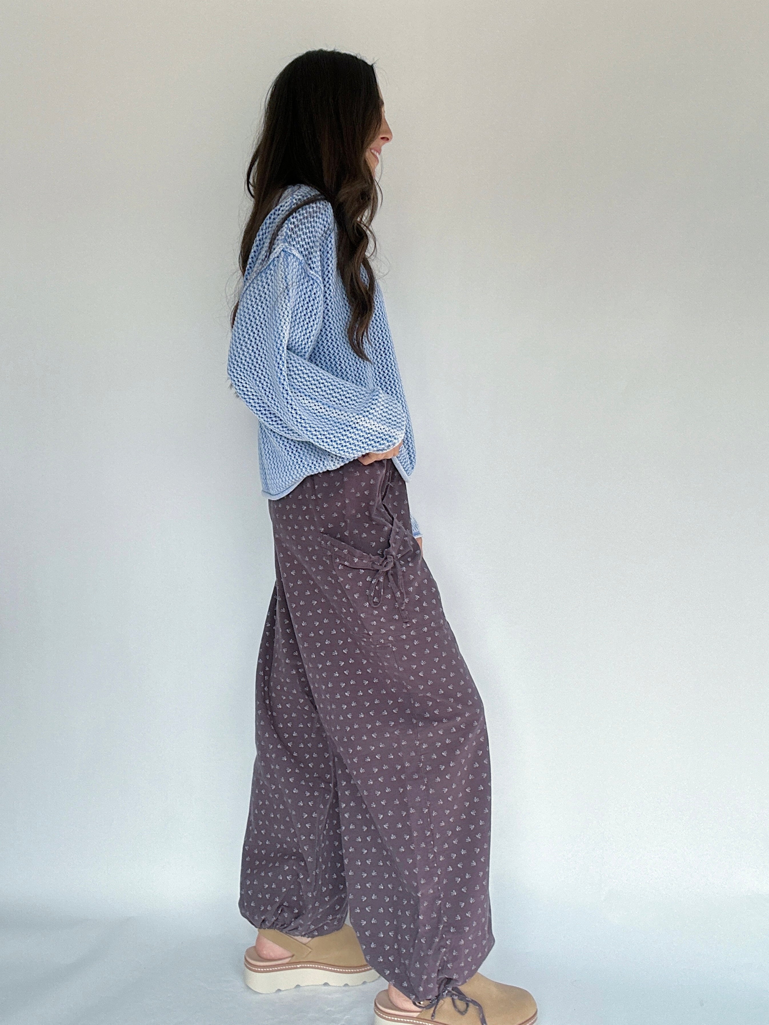 Person wearing a blue knitted sweater and patterned pants against a white background showing side view